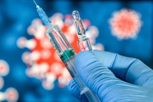 Bilde av en hånd, med engangshanske på, som holder en vaksine. I bakgrunnen er det en uklar illustrasjon av et koronavirus. Foto: Mostphotos.