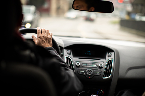 Bildet er tatt fra baksetet i en bil. En person sitter i førersetet og kjører bilen. Foto: Mostphotos.