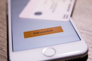 Bilde av en mobiltelefon hvor førerkortappen er åpen. Oppå telefonen ligger et fysisk førerkort. Foto: Mostphotos.
