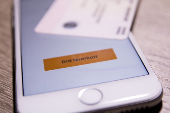 Bilde av en mobiltelefon hvor førerkortappen er åpen. Oppå telefonen ligger et fysisk førerkort. Foto: Mostphotos.