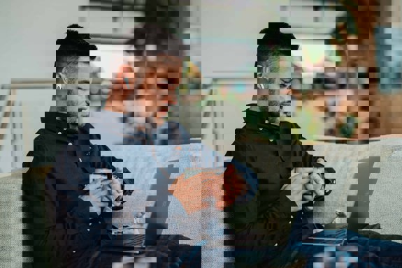 Ein person sit i sofaen med PC på fanget og kaffikopp i handa. Foto: Unsplash.