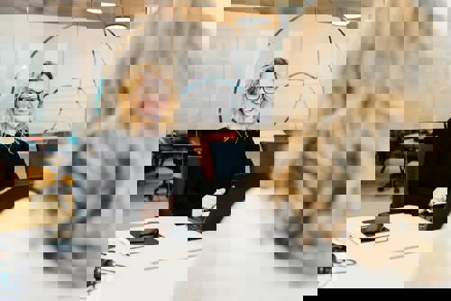 To kvinner sit i eit møte. Ei sit med ryggen til, og den andre ser mot kamera og smiler. Foto: Cecilie Bannow.