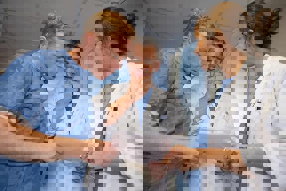 Tre helsepersonell står og ser på et papir og snakker sammen sammen. Foto: Mostphotos.