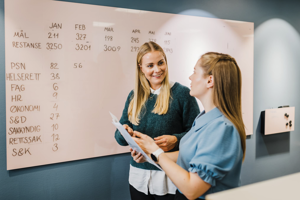 To smilende kvinner foran en tavle.