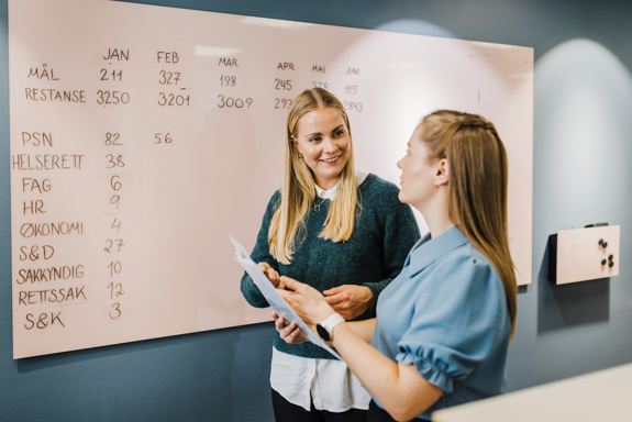 To smilende kvinner foran en tavle.