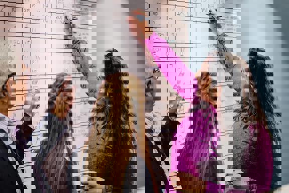 Tre personer foran en tavle, en skriver på tavlen. Foto: Cecilie Bannow.